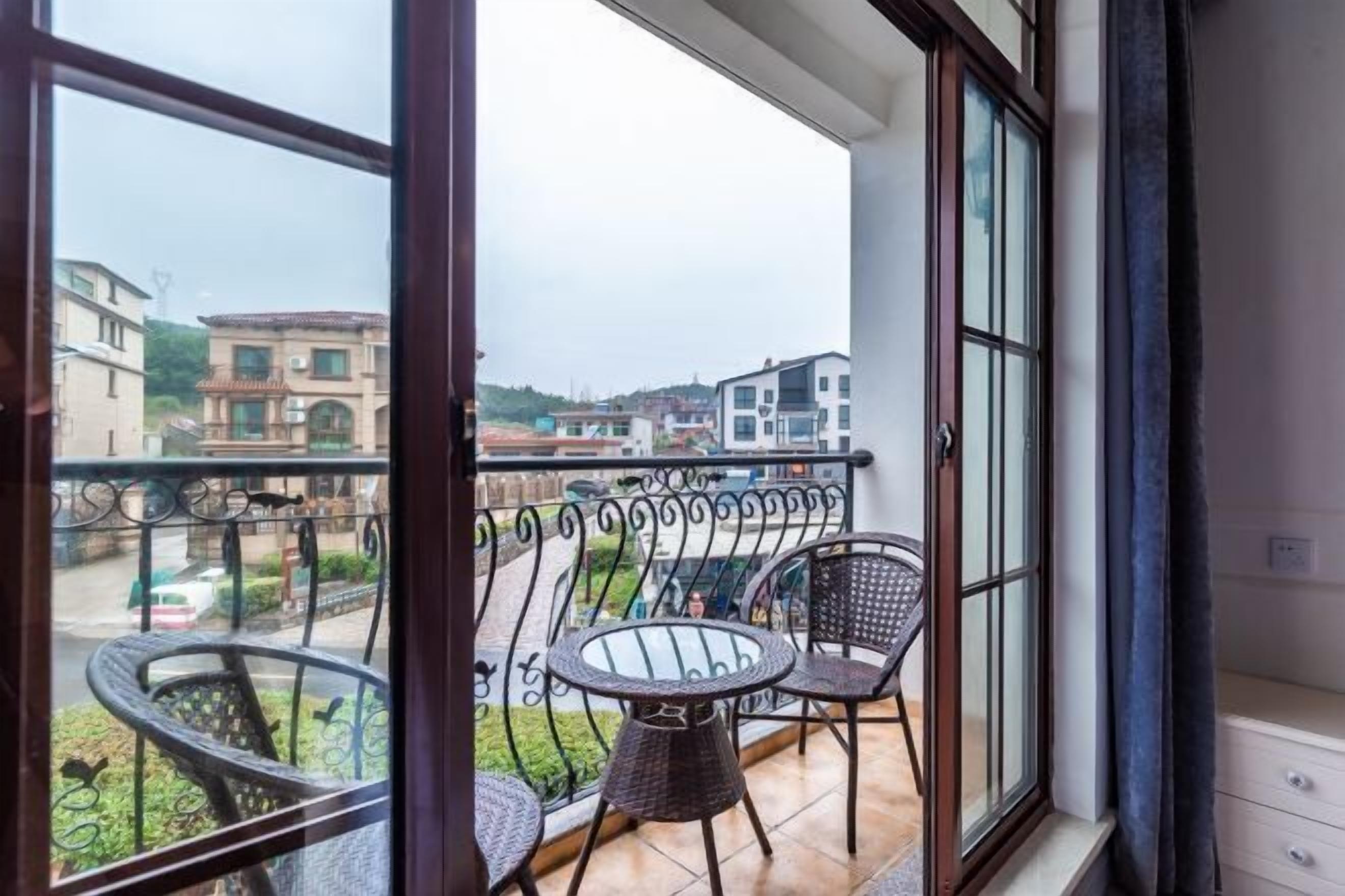 A balcony with wicker chairs and a table, overlooking a residential area with buildings.