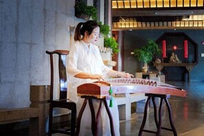 A person playing a stringed musical instrument in a room with a stone wall and a wooden chair. - Suzhou Yuanqu Xinghai SCHOLARS Hotel (Jinji Lake) (Suzhou)