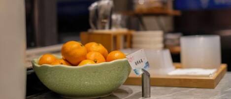 A green bowl filled with oranges on a marble countertop, with a small sign next to it.