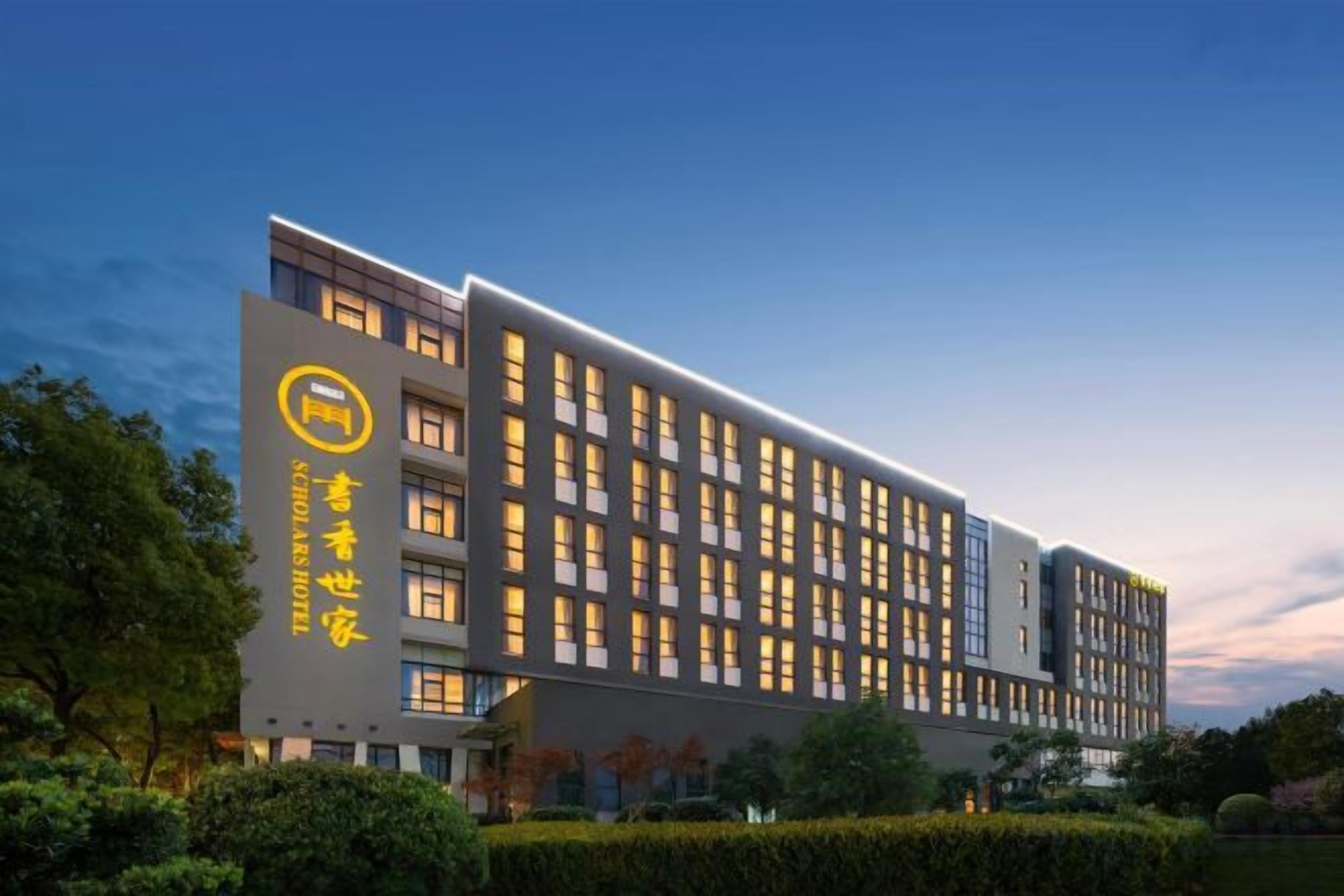 A modern hotel building with multiple floors, large windows, and a prominent logo on the facade.