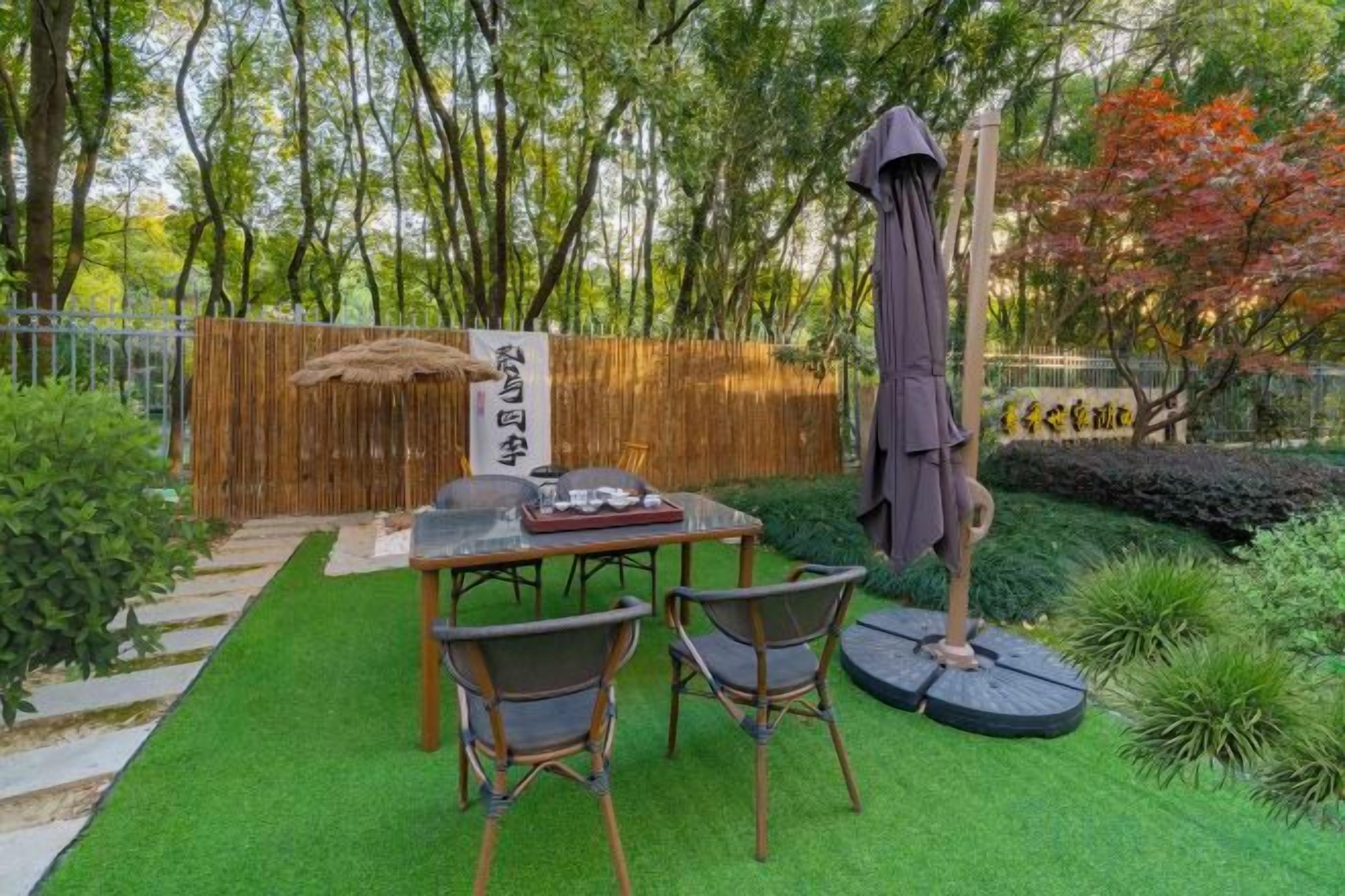 An outdoor seating area with a table and chairs, surrounded by greenery and a bamboo fence.