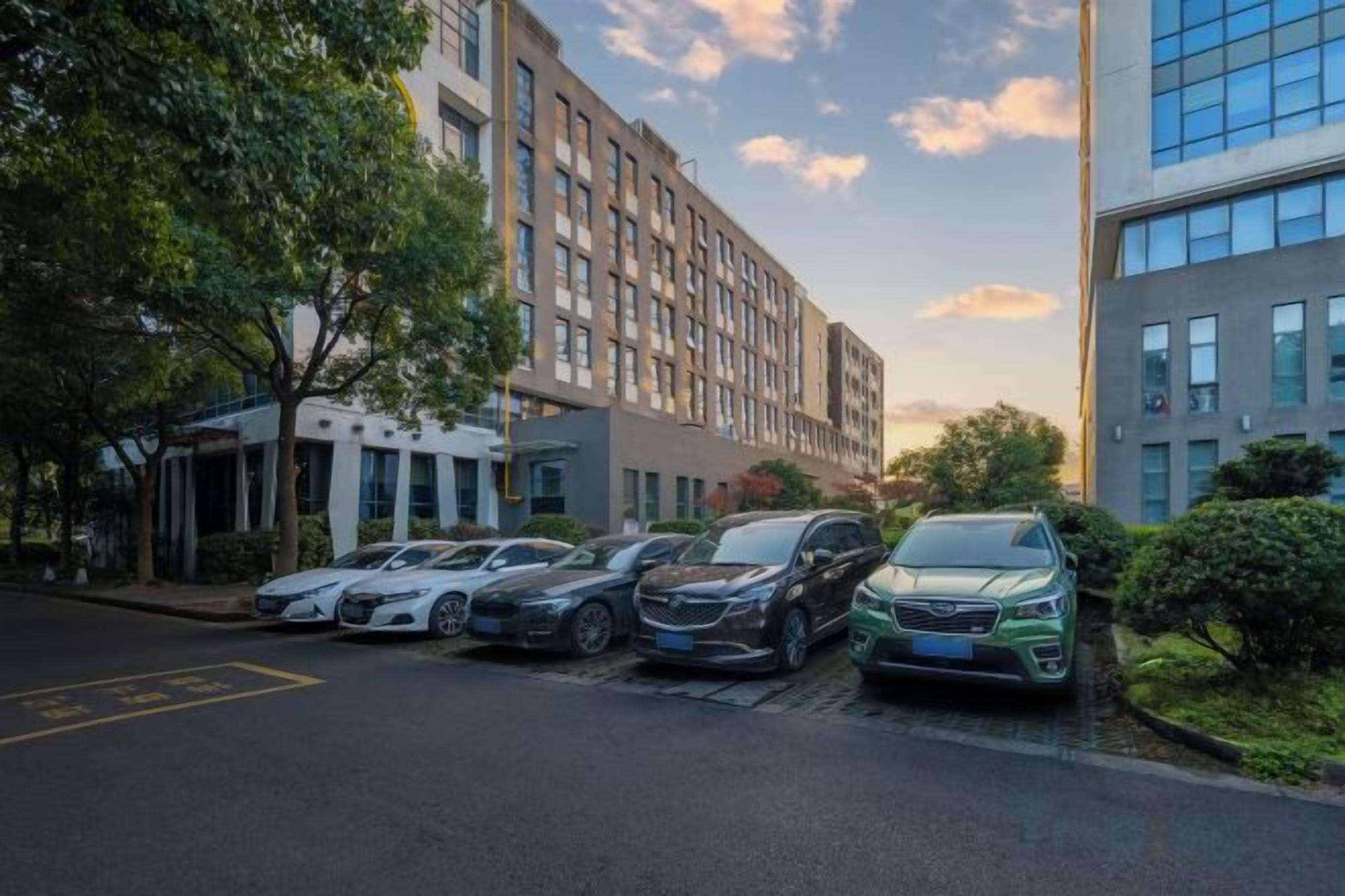 A parking lot with several cars, a building with multiple floors, and a clear sky.
