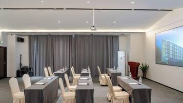 A conference room with rows of tables and chairs, a projector, and a large screen.