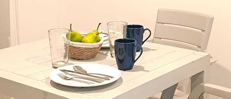 Una mesa de comedor blanca con un plato, cubiertos, una copa, una taza azul y una cesta de limones.