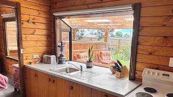 Cocina compacta con paredes de madera, una ventana, un fregadero, un tostador, una estufa y una pequeña zona de encimera.