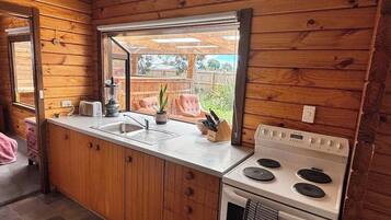 Eine kleine Küche mit Holzwänden, einem Fenster, einer Spüle, einem Herd und einer Arbeitsplatte mit Toaster und Pflanze.