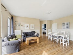Un salon avec un canapé gris, une table basse en bois et un coin repas comprenant des chaises et une table blanches.