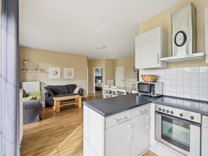 A modern kitchen with white cabinets, a microwave, and a stove. - Cozy holiday apartment with terrace and garden. (Bastorf)