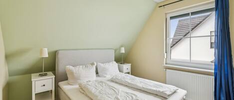 Una camera da letto con un letto, comodini, una finestra con tende e un termosifone.