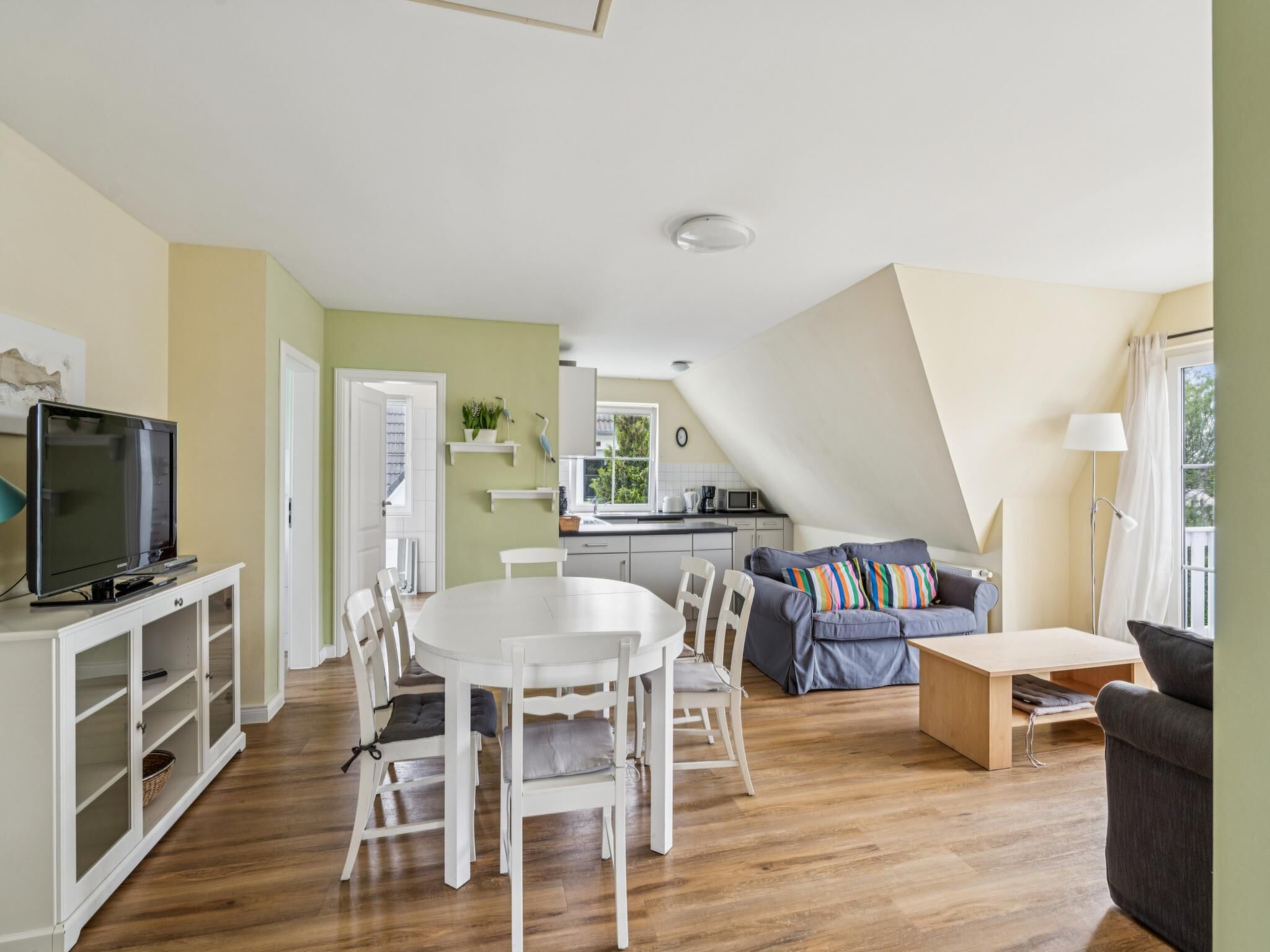 Uma sala de estar moderna com área de jantar, cozinha compacta e um mezanino com quarto e janela.