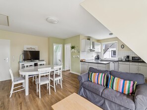 A modern apartment with a dining area, a gray sofa with colorful cushions, a kitchen with white cabinets, and a small dining table. - Beachfront vacation apartment near Kühlungsborn (Bastorf)