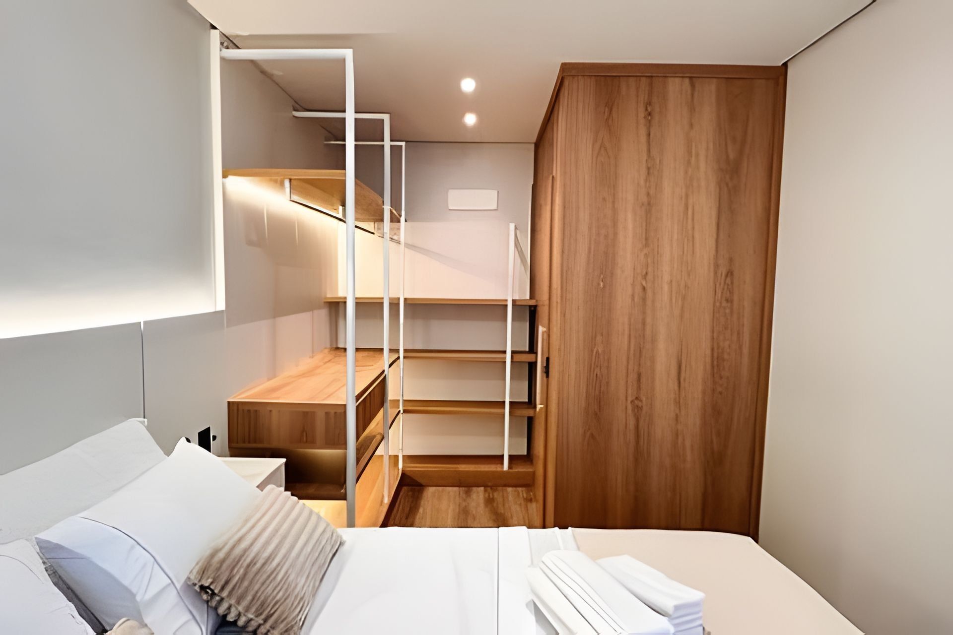 A modern bedroom with a bed, a wooden wardrobe, and a built-in shelving unit.
