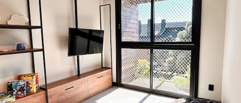 A modern living room with a large window, a flat-screen TV, wooden furniture, and a bean bag.