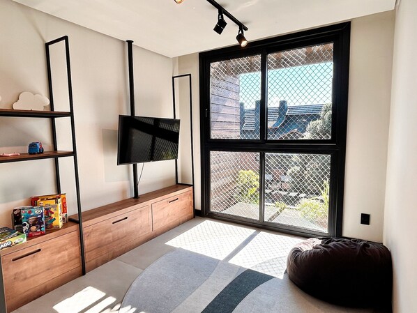 A modern living room with a large window, a flat-screen TV, wooden furniture, and a bean bag.