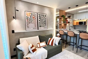 A modern living room with a sofa, a dining area with chairs, and a kitchen in the background.