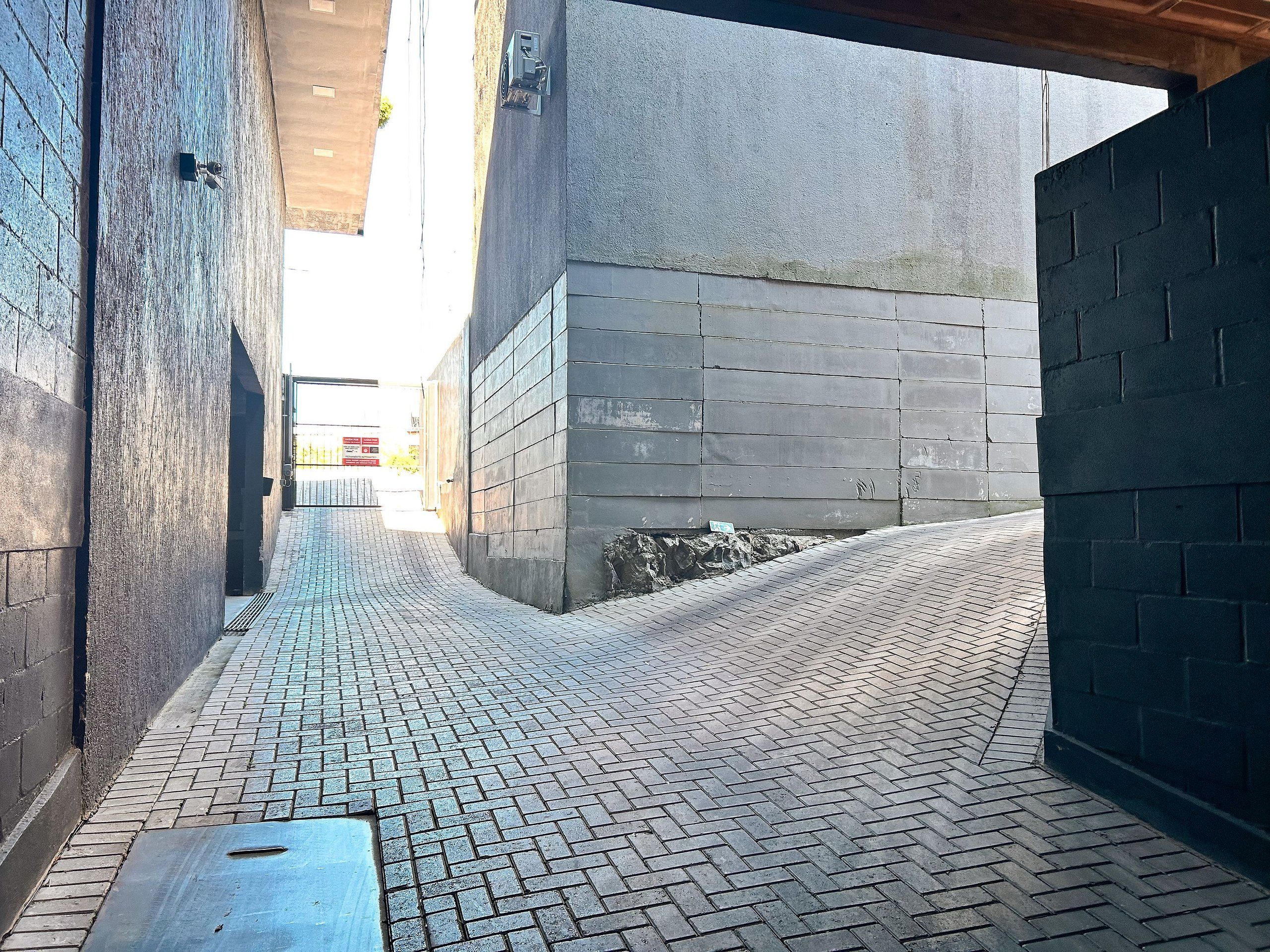 A narrow alleyway with a brick floor, a concrete wall on the right, and a metal door on the left.