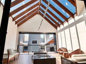 An interior space with a sloped ceiling, a seating area with chairs and a sofa, and a view through a glass door to an outdoor area. - A dois passos de tudo (Canela)