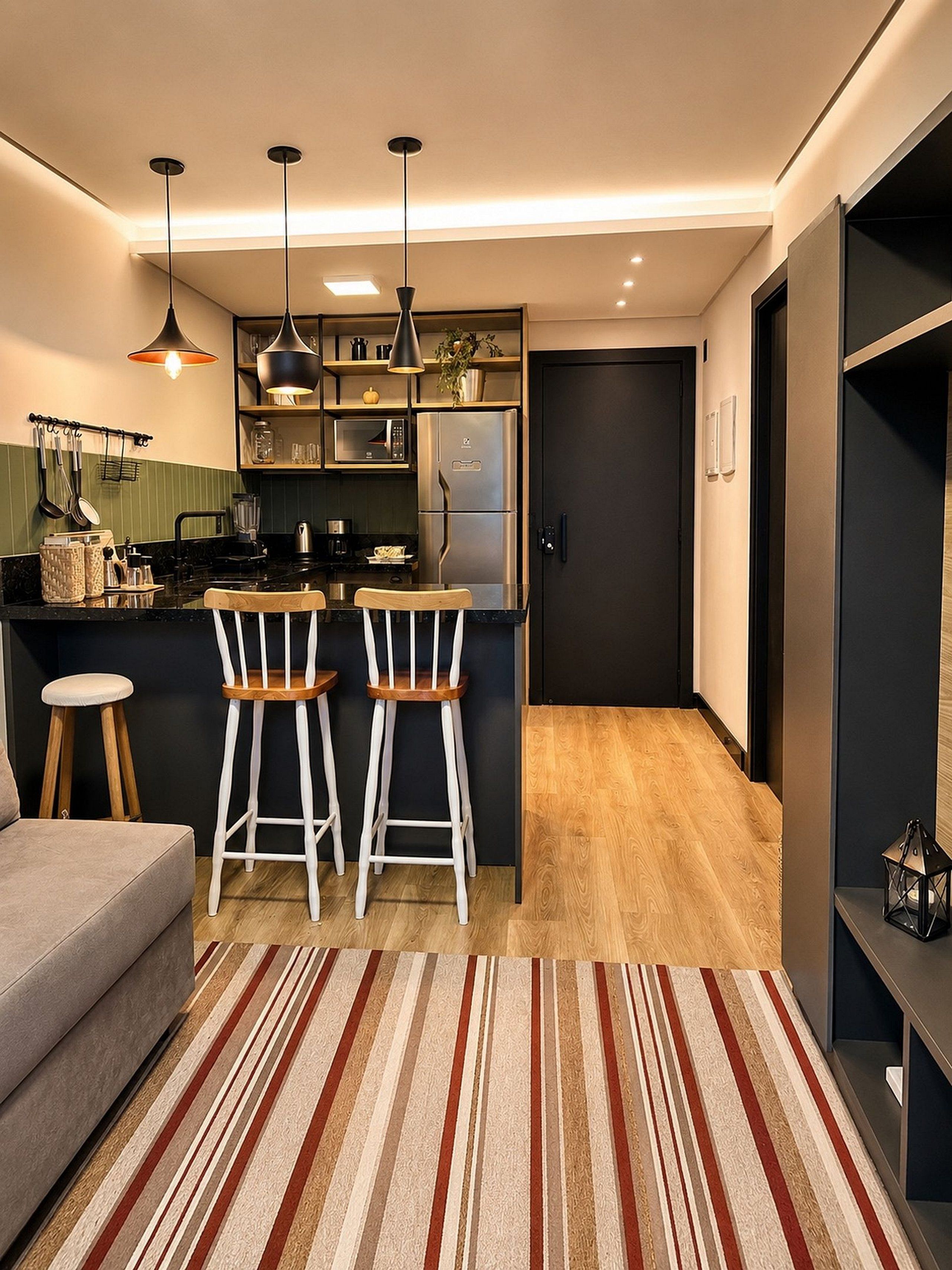 Cocina compacta con isla central, dos taburetes de bar, refrigerador e iluminación colgante.