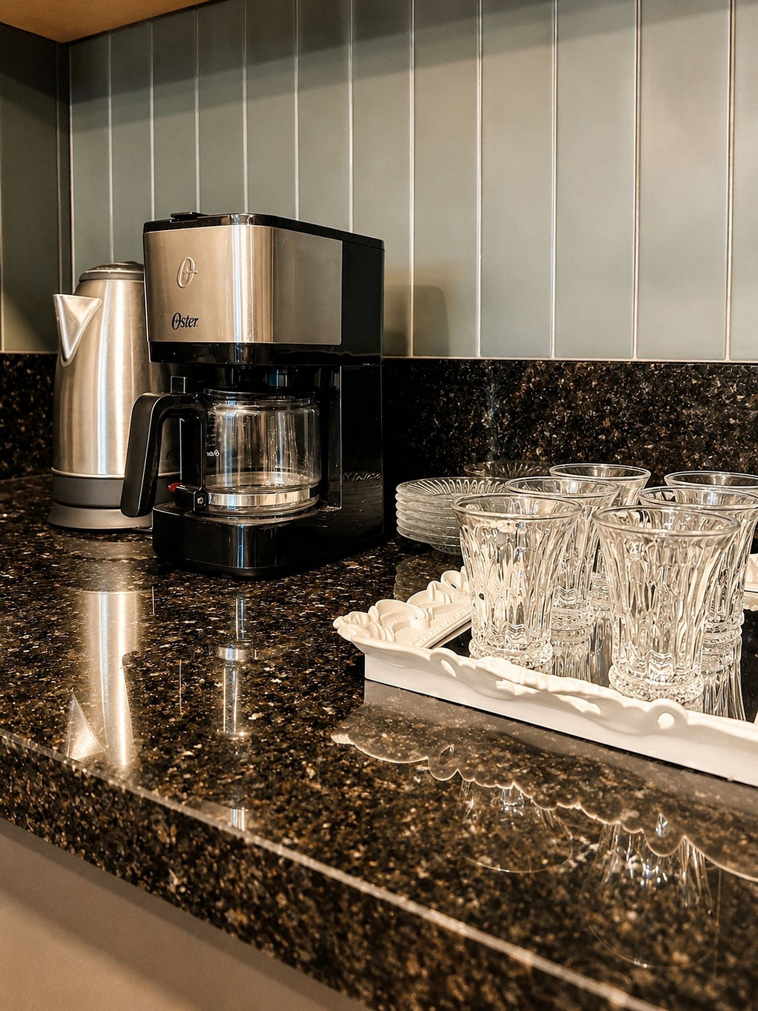 A kitchen with a coffee maker, a kettle, and a tray of glasses.