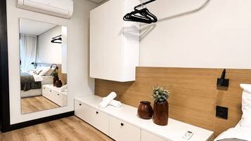 Habitación de hotel moderna con cabecera de madera, una mesita de noche con un florero y un control remoto, un espejo grande y una lámpara colgante.