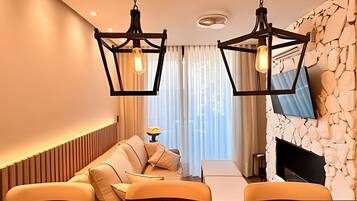 A modern living room with a sofa, a flat-screen TV mounted on a stone wall, and pendant lighting.
