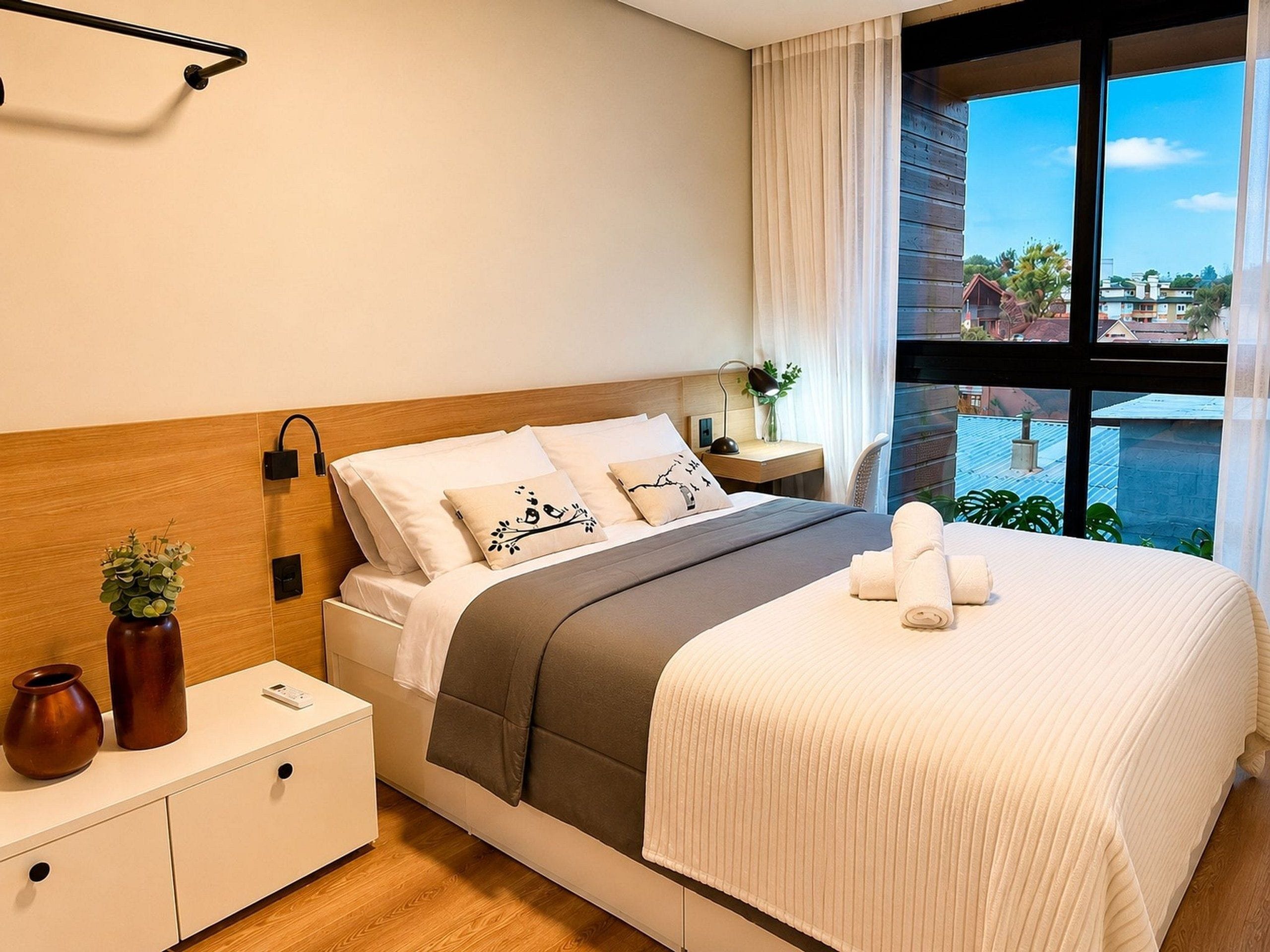 Habitación de hotel con cama, mesita de noche, lámpara y vistas amplias de la ciudad.