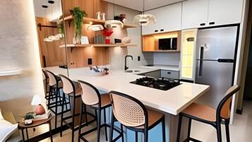 Una cocina moderna con una isla central, taburetes de bar, iluminación colgante y electrodomésticos de acero inoxidable.