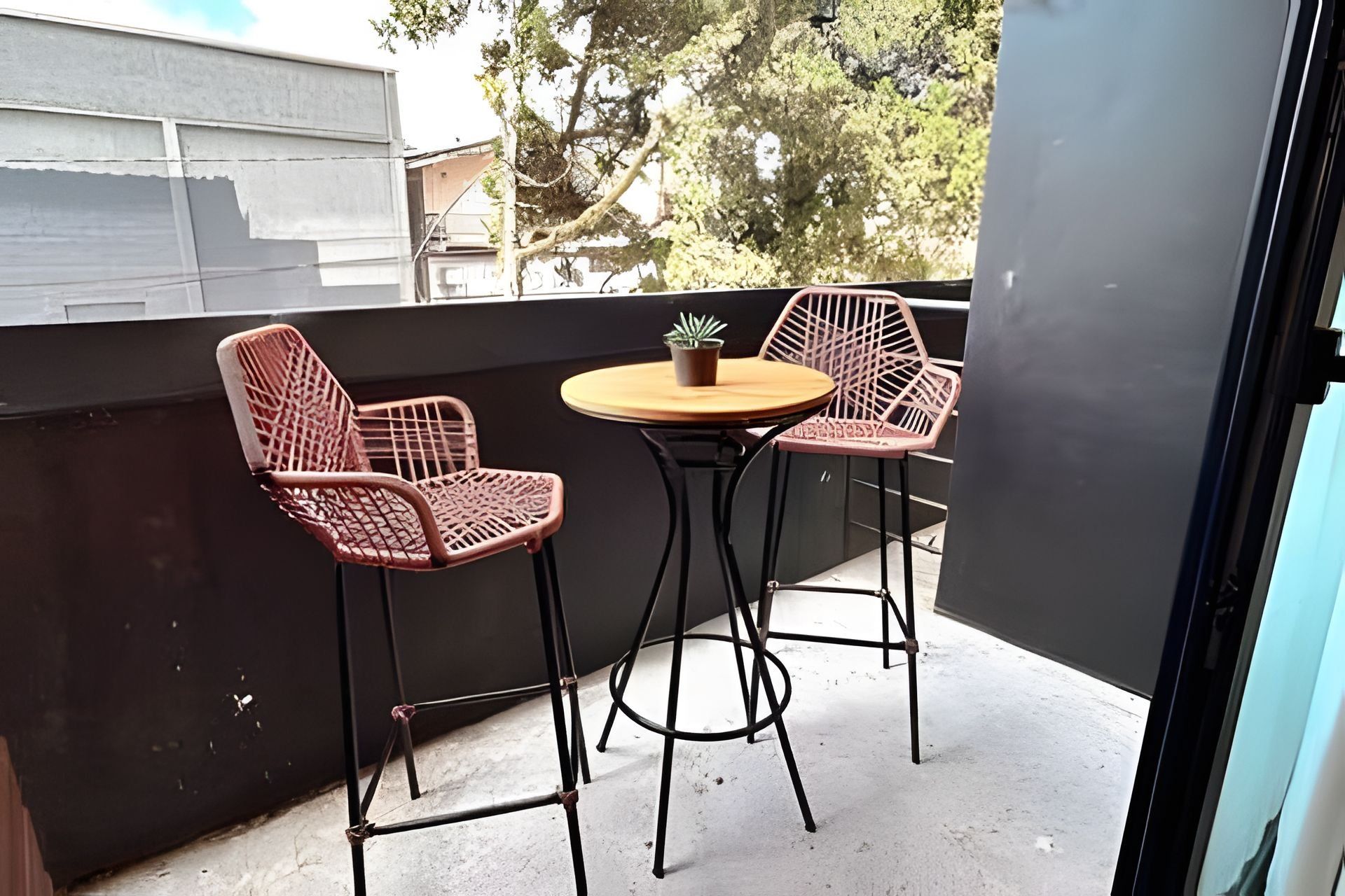 A balcony with two chairs and a small table, a potted plant, and a view of trees and buildings.