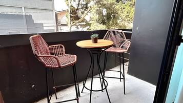A balcony with two chairs and a small table, a potted plant, and a view of trees and buildings.