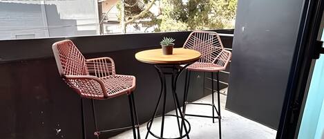 A balcony with two chairs and a small table, a potted plant, and a view of trees and buildings.