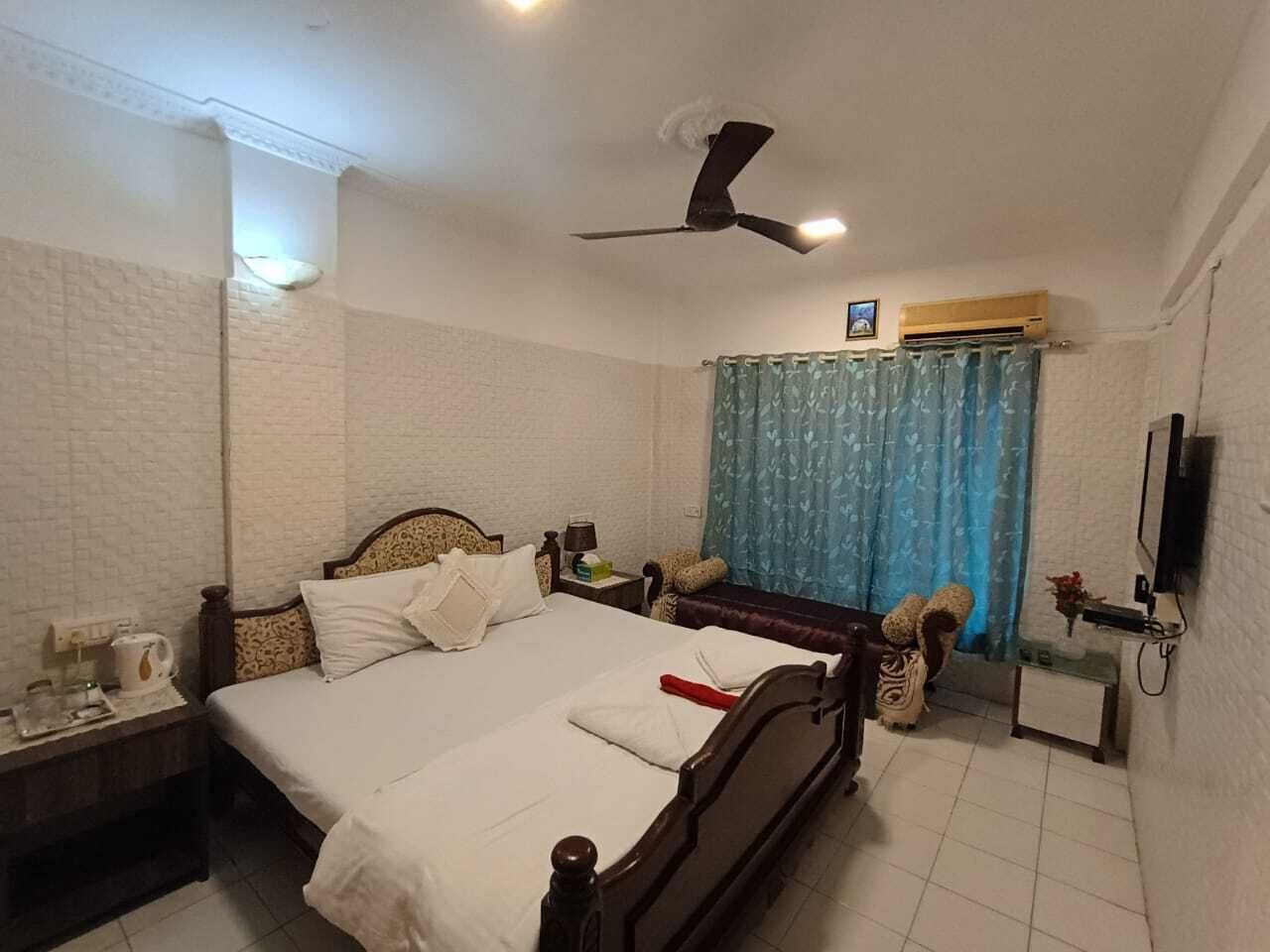 Quarto de hotel com cama, mesa de cabeceira, abajur, ar condicionado e ventoinha no teto.