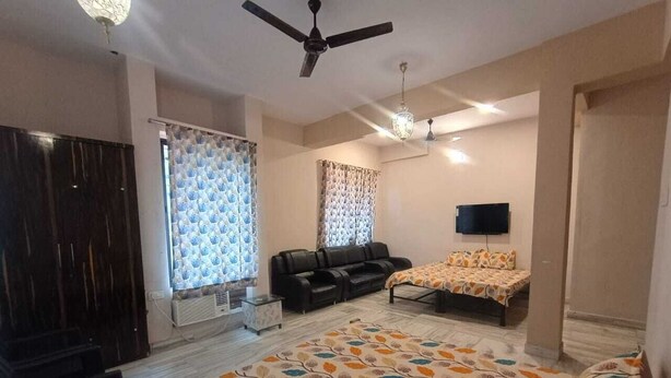 A bedroom with a bed, a sofa, a TV, and a ceiling fan.