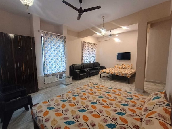 A bedroom with a bed, a sofa, a TV, and a ceiling fan.