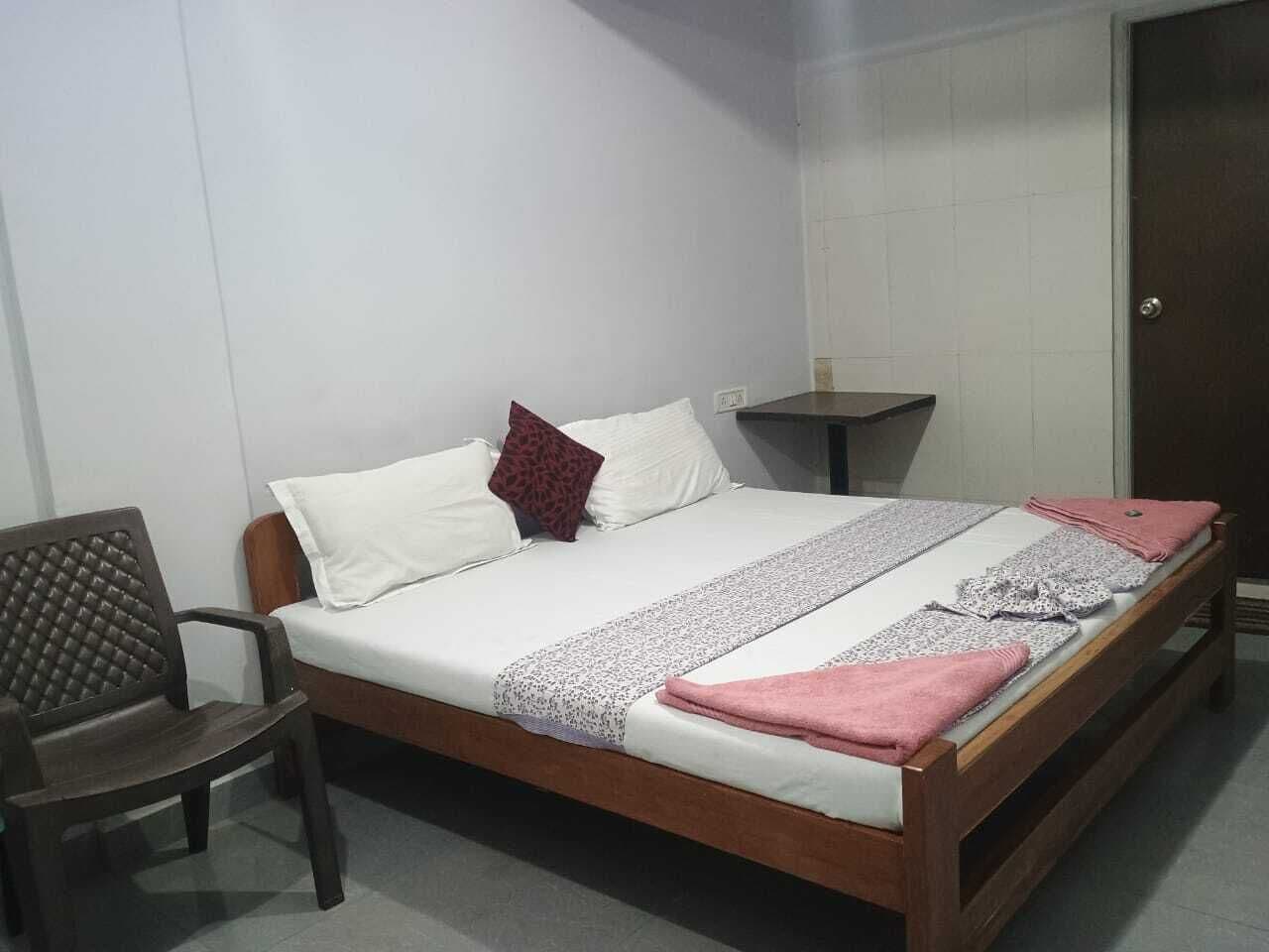 A single bed with a wooden frame, white bedding, and a patterned throw. A chair is positioned to the left of the bed.