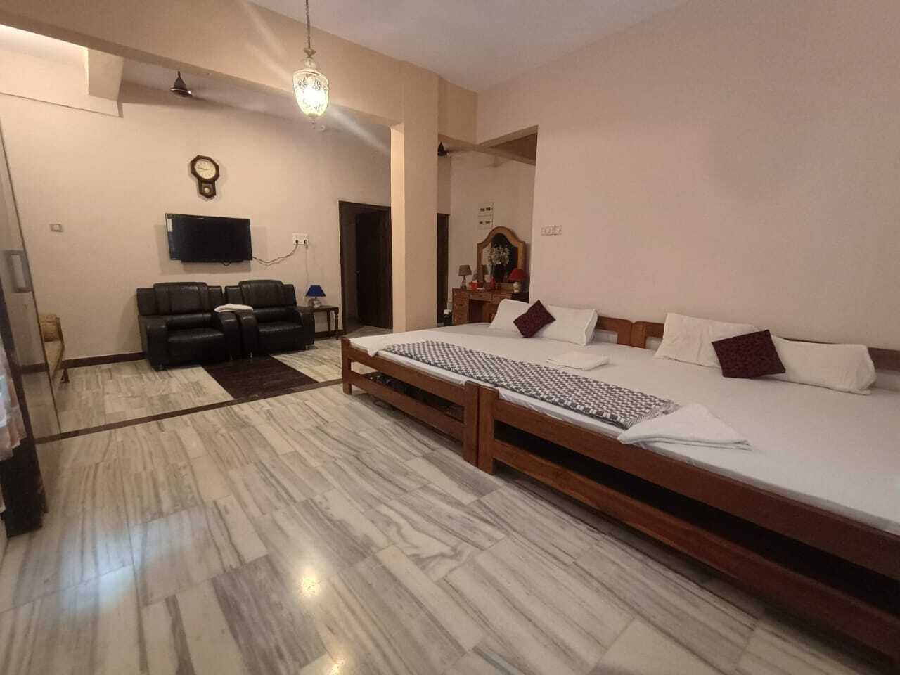 A bedroom with a large bed, a TV, a clock, and a sofa.