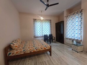 A bedroom with a bed, a ceiling fan, a desk, and two chairs.