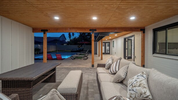 An outdoor seating area with a pool, wooden ceiling, and a view of a house in the background. - Spacious high-end, newly remodeled 5-bedroom house in delightful Gilbert. (Gilbert)