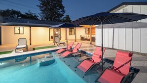 A swimming pool with lounge chairs and an umbrella, surrounded by a building with a covered patio area. - Spacious high-end, newly remodeled 5-bedroom house in delightful Gilbert. (Gilbert)
