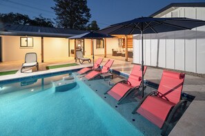 A swimming pool with lounge chairs and an umbrella, surrounded by a building with a covered patio area. - Spacious high-end, newly remodeled 5-bedroom house in delightful Gilbert. (Gilbert)