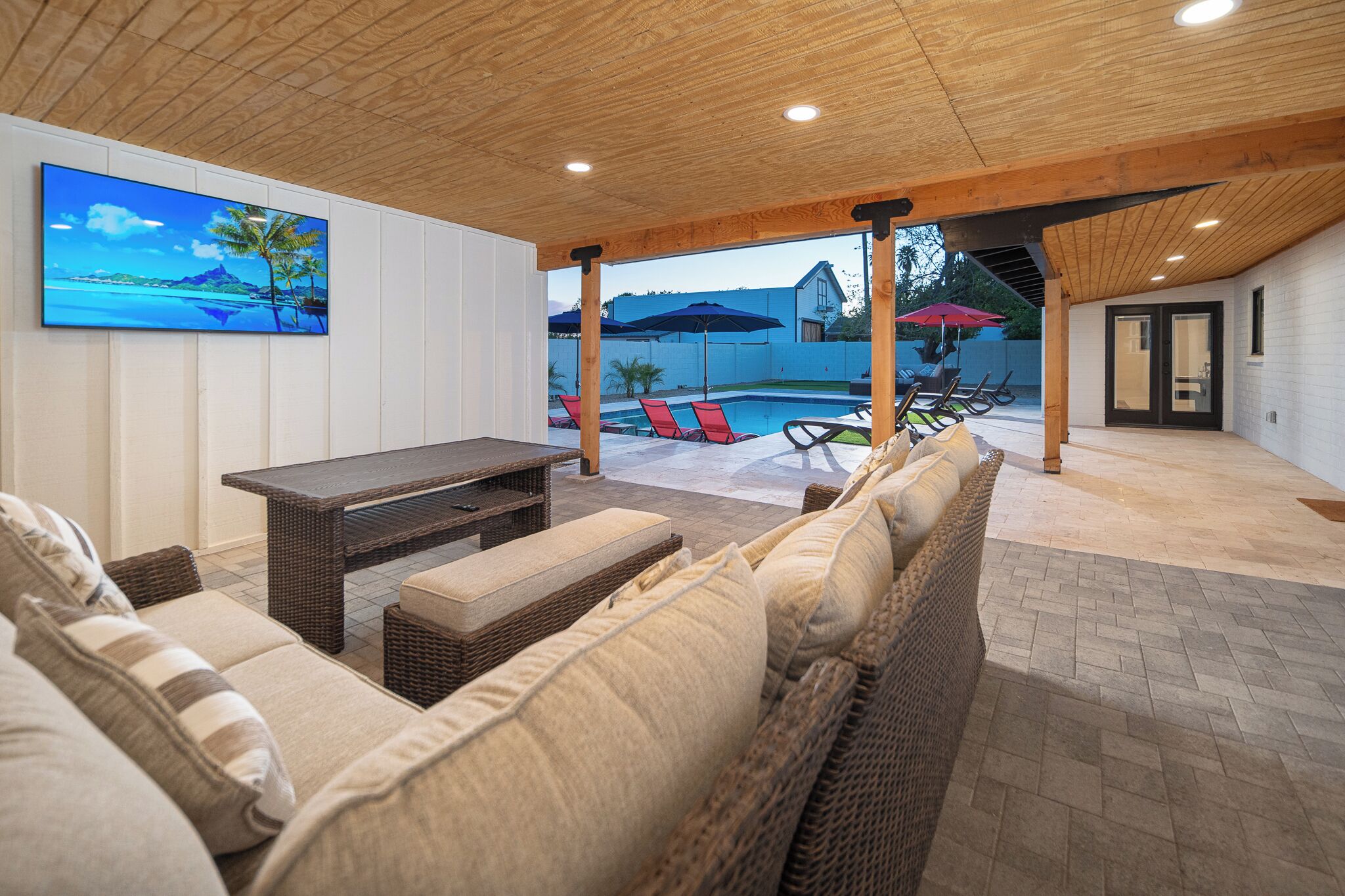 An outdoor patio with wicker furniture, a pool, and umbrellas.