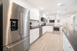 A modern kitchen with stainless steel appliances, white cabinetry, and a wooden floor. - Spacious high-end, newly remodeled 5-bedroom house in delightful Gilbert. (Gilbert)