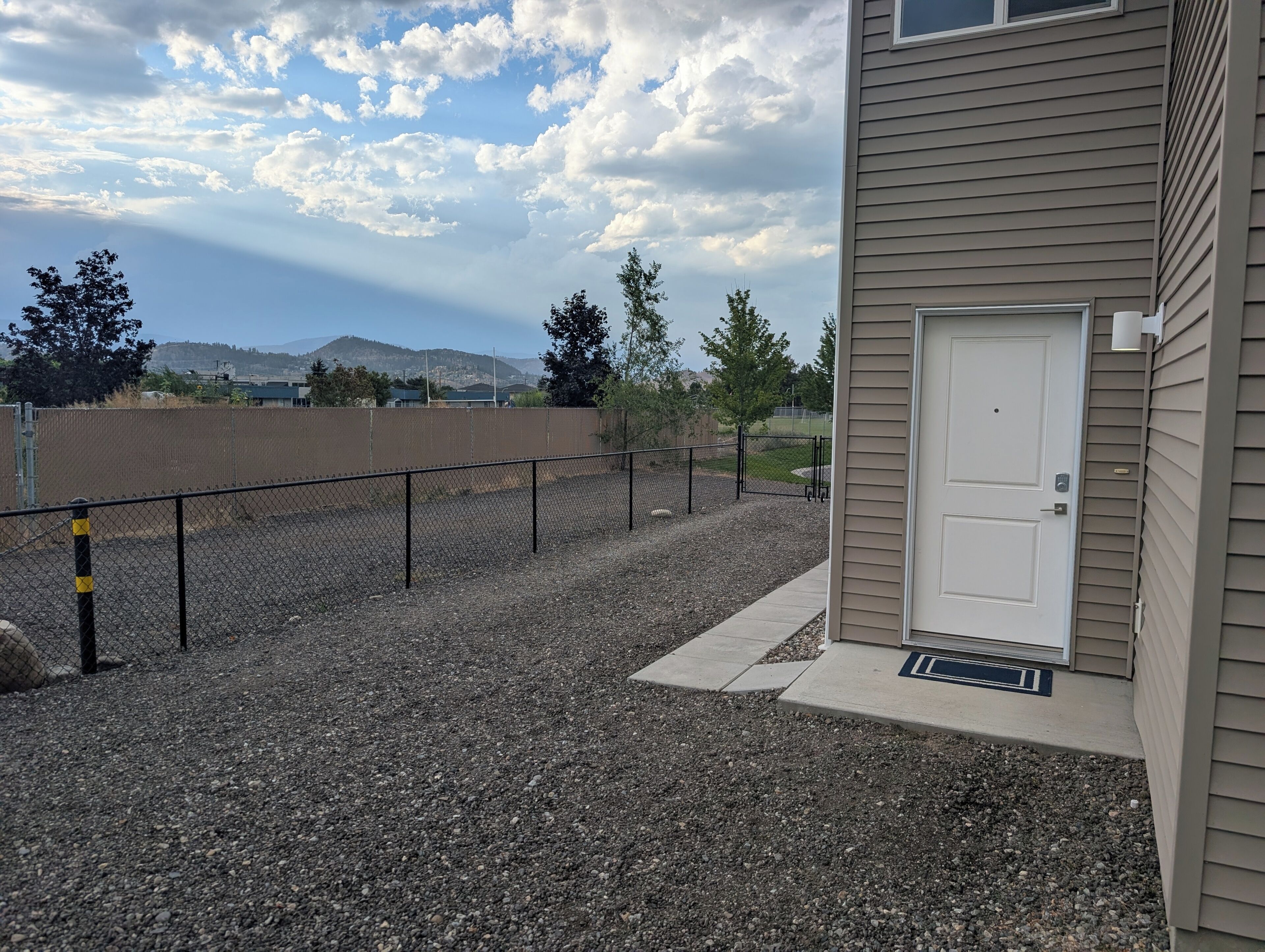 A building with a white door, a gravel driveway, and a chain-link fence.