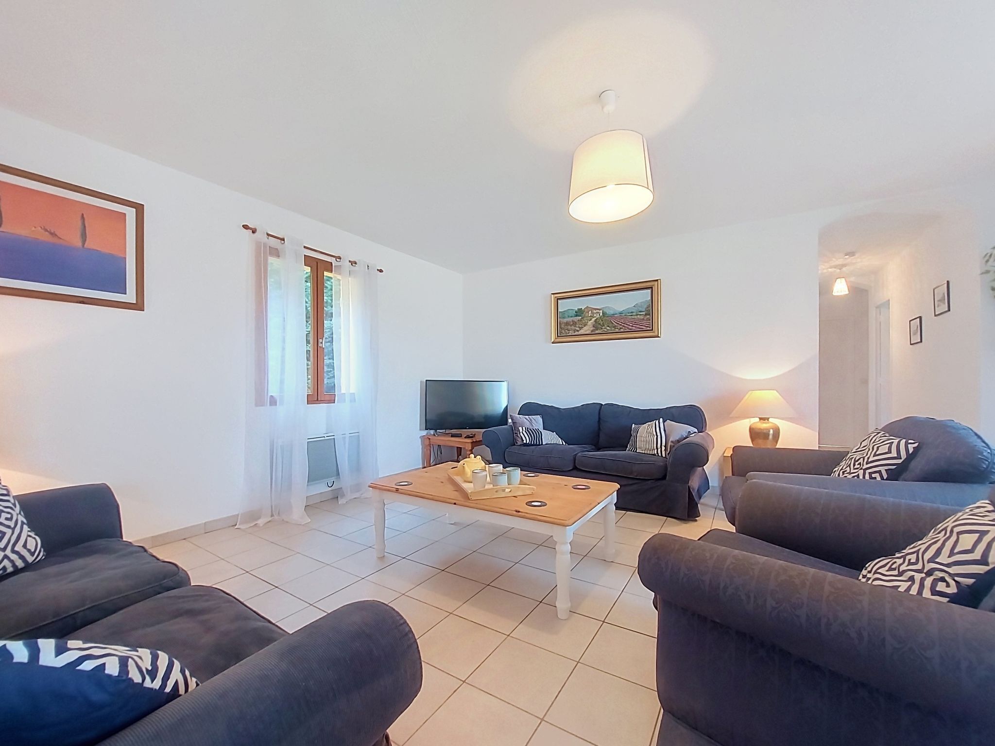 Un salon comprenant un canapé, une table basse, un téléviseur et un tableau accroché au mur.