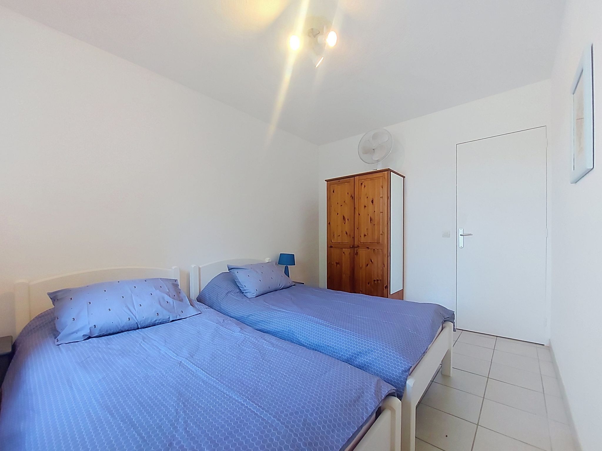 A bedroom with two beds, a wooden wardrobe, a white door, and a ceiling fan.
