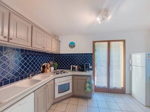 A kitchen with white cabinets, a blue tiled backsplash, a stove, a sink, and a refrigerator. - La Jeansarde by Interhome (Fox-Amphoux)