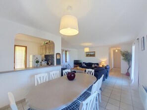 A modern kitchen with white cabinets, a dining area with a round table and chairs, and a living room with a sofa and a TV. - La Jeansarde by Interhome (Fox-Amphoux)