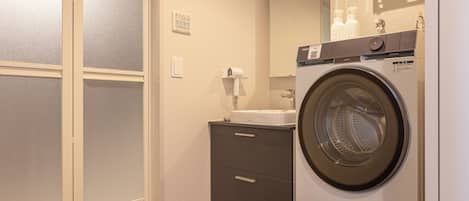 A compact hotel bathroom with a washing machine, a sink, and a mirror.