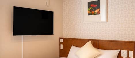 A hotel room with a bed, a flat-screen TV mounted on the wall, and an air conditioning unit.