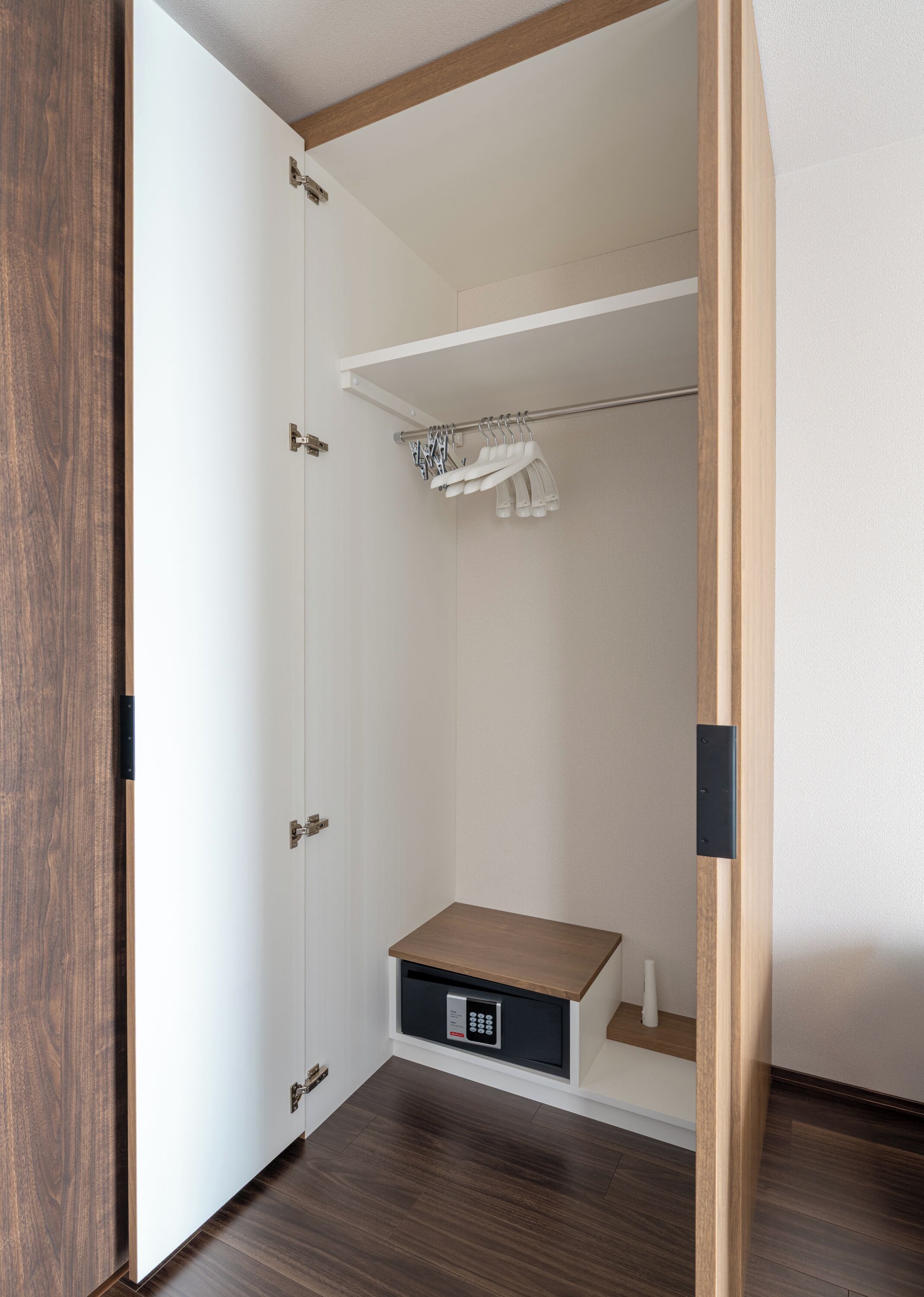 A walk-in closet with a wooden floor, a hanging rod, and a built-in shoe rack.