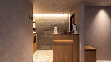 A hotel reception area with a wooden reception desk, a small seating area, and a wall-mounted sign indicating amenities.